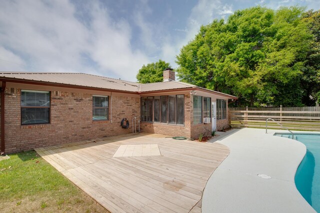 rear view of property with metal roof, a chimney, a wooden deck, brick siding, and fence