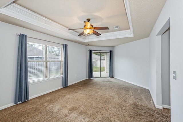 carpeted empty room featuring ceiling fan, visible vents, crown molding, a raised ceiling, and baseboards