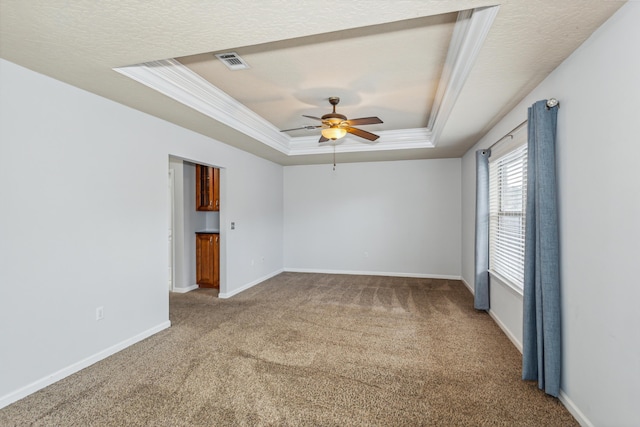 carpeted empty room with a ceiling fan, visible vents, crown molding, baseboards, and a tray ceiling