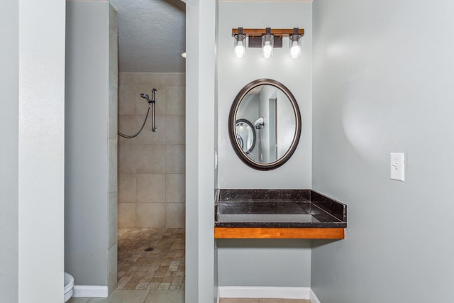 bathroom with baseboards, tile patterned flooring, a tile shower, and toilet