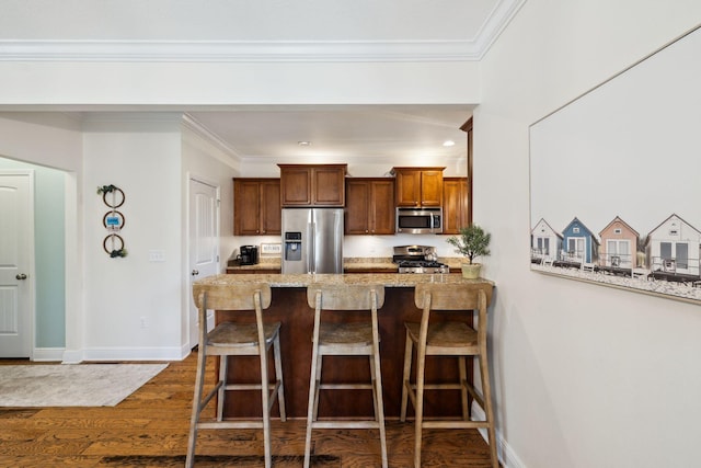 kitchen featuring appliances with stainless steel finishes, dark wood-type flooring, a kitchen breakfast bar, crown molding, and brown cabinets
