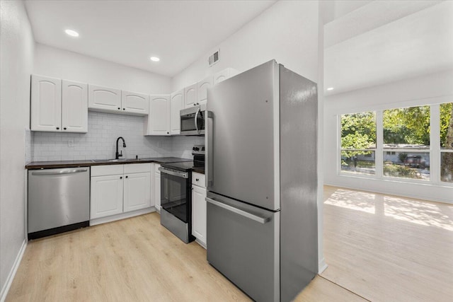 kitchen featuring dark countertops, light wood-style floors, white cabinets, a sink, and appliances with stainless steel finishes