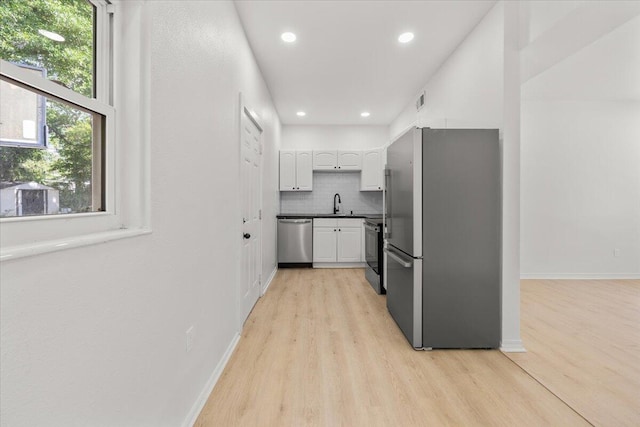 kitchen with dark countertops, white cabinetry, tasteful backsplash, light wood finished floors, and appliances with stainless steel finishes