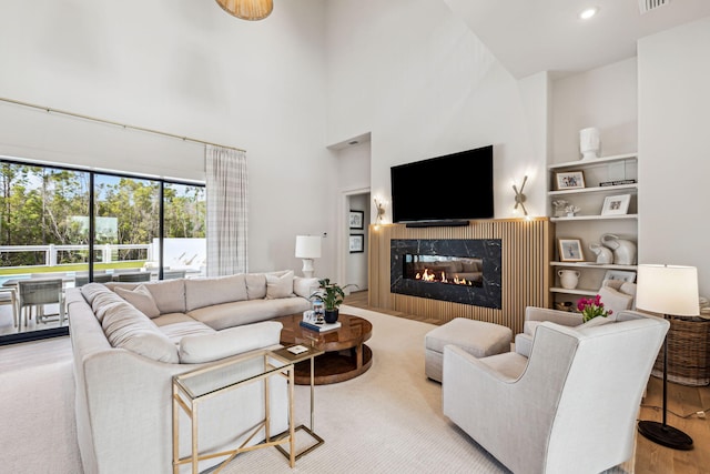 living area featuring a glass covered fireplace, a high ceiling, recessed lighting, and wood finished floors