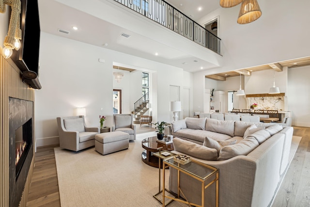 living room featuring visible vents, wood finished floors, stairway, a warm lit fireplace, and a high ceiling
