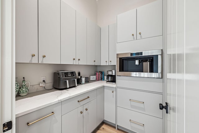 kitchen featuring white cabinetry, light stone counters, and light wood-style flooring