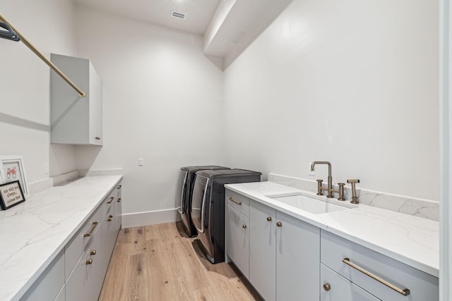 washroom featuring washing machine and dryer, baseboards, cabinet space, a sink, and light wood-style flooring