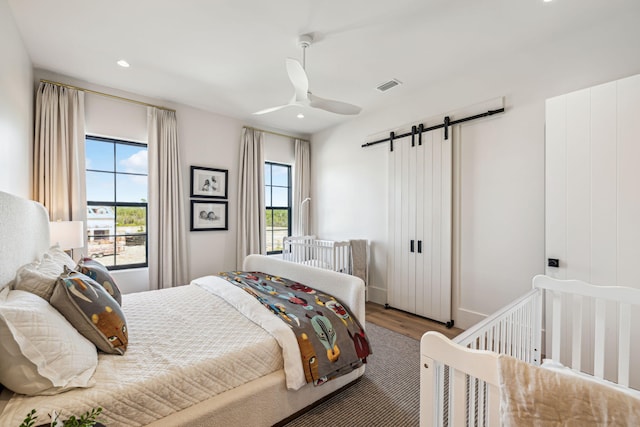 bedroom featuring a barn door, a ceiling fan, recessed lighting, wood finished floors, and visible vents