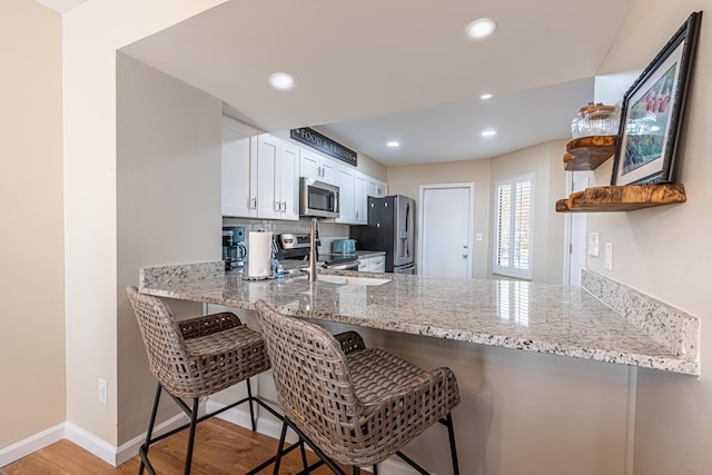kitchen with open shelves, a peninsula, light stone countertops, light wood-style flooring, and appliances with stainless steel finishes