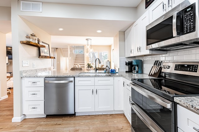 kitchen with appliances with stainless steel finishes, a sink, light wood finished floors, recessed lighting, and white cabinetry
