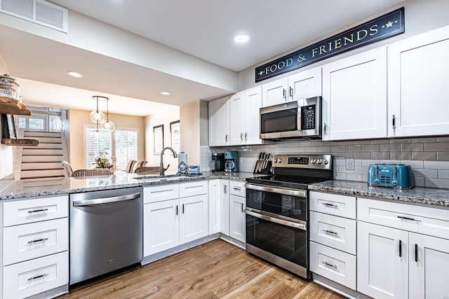 kitchen featuring visible vents, a peninsula, white cabinets, a sink, and appliances with stainless steel finishes
