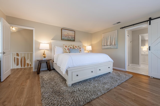 bedroom with a barn door, baseboards, wood finished floors, and visible vents