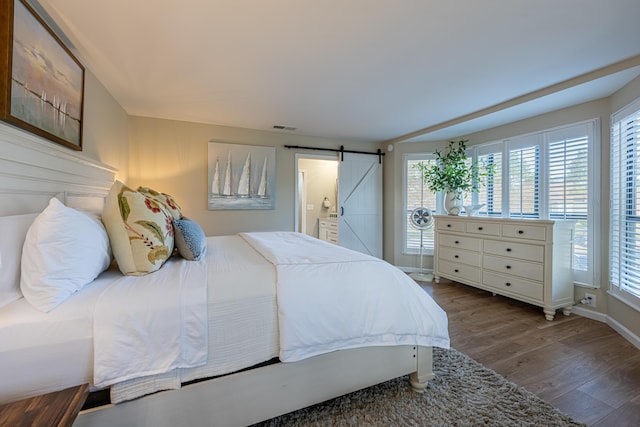 bedroom with visible vents, a barn door, wood finished floors, and multiple windows