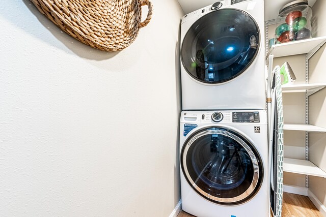 laundry area featuring baseboards, laundry area, stacked washer / drying machine, and wood finished floors