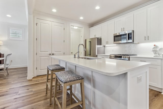 kitchen featuring a center island with sink, a kitchen bar, white cabinetry, light wood finished floors, and appliances with stainless steel finishes