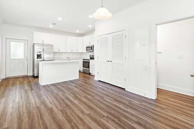 kitchen with appliances with stainless steel finishes, ornamental molding, light countertops, white cabinetry, and wood finished floors