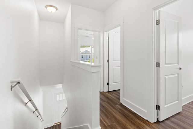 corridor featuring an upstairs landing, dark wood-type flooring, and baseboards