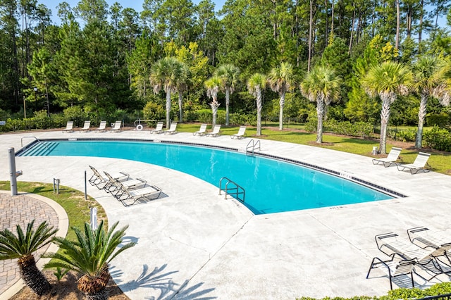 community pool featuring view of wooded area and a patio area