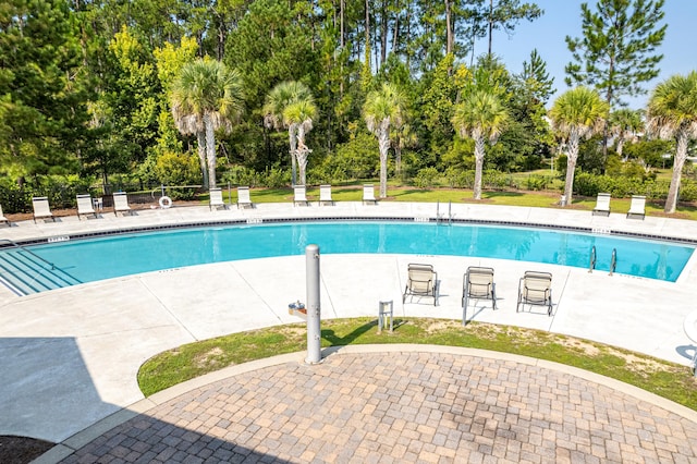 community pool with view of wooded area and a patio