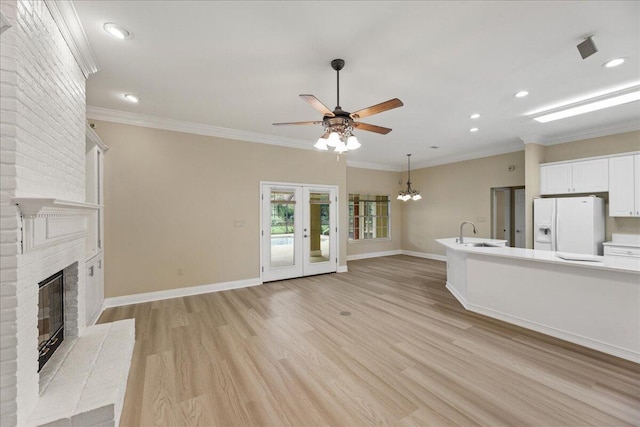 unfurnished living room featuring crown molding, a fireplace, a sink, ceiling fan with notable chandelier, and light wood-style floors