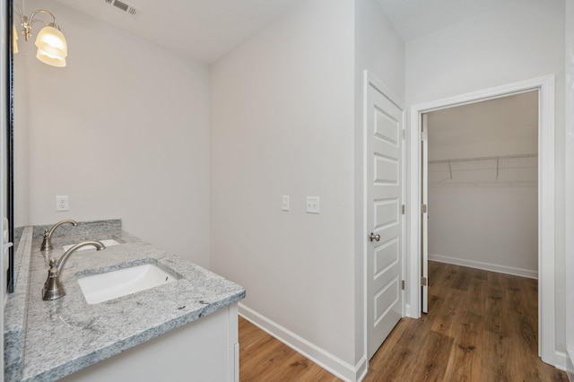 bathroom with double vanity, wood finished floors, a sink, visible vents, and baseboards