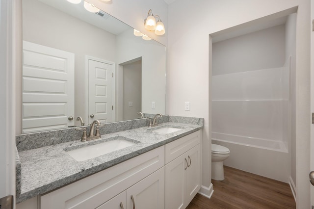 bathroom featuring toilet, double vanity, a sink, and wood finished floors