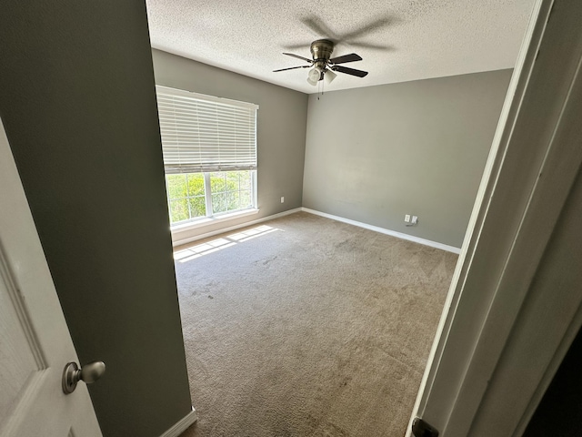 carpeted spare room featuring baseboards, a ceiling fan, and a textured ceiling