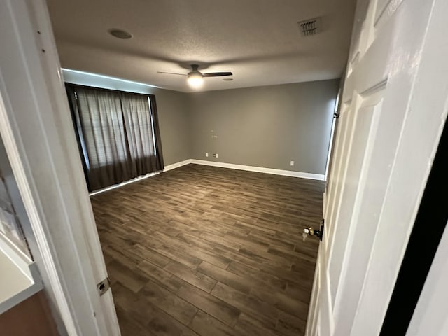 spare room with ceiling fan, visible vents, baseboards, and dark wood-type flooring