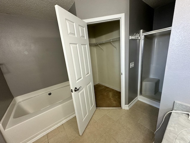 full bathroom featuring a walk in closet, tile patterned floors, baseboards, a bath, and a stall shower