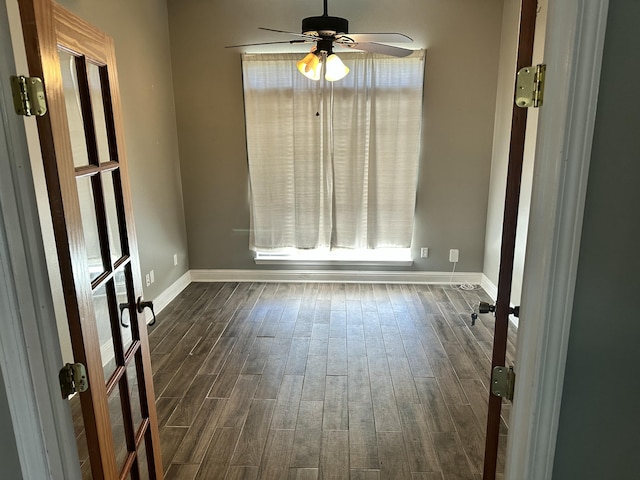 empty room featuring dark wood-type flooring, baseboards, and ceiling fan