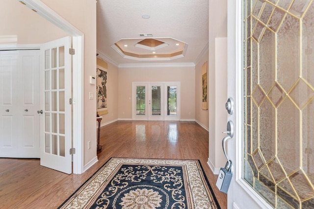 foyer featuring french doors, a raised ceiling, ornamental molding, wood finished floors, and baseboards