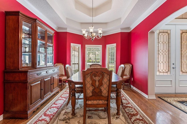 dining room with a chandelier, wood finished floors, a tray ceiling, and baseboards