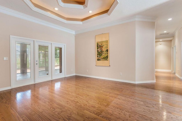 unfurnished room with wood finished floors, french doors, ornamental molding, a tray ceiling, and baseboards