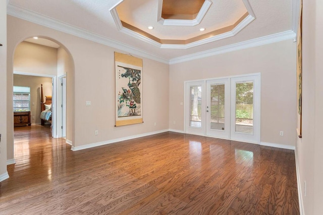 unfurnished room featuring a raised ceiling, wood finished floors, arched walkways, ornamental molding, and baseboards