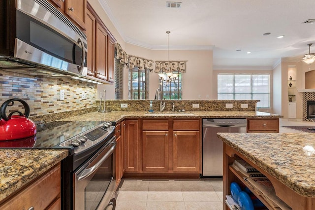 kitchen featuring appliances with stainless steel finishes, a sink, brown cabinetry, decorative backsplash, and ornamental molding