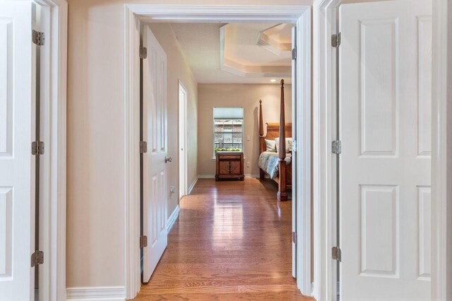 hall with light wood-type flooring, a tray ceiling, and baseboards