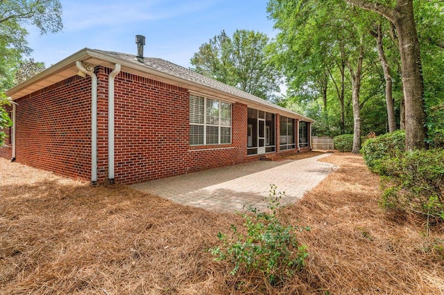 back of property with a sunroom, brick siding, a patio, and fence