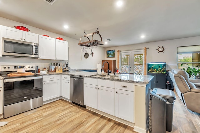 kitchen with appliances with stainless steel finishes, a sink, a peninsula, open floor plan, and light wood-style floors