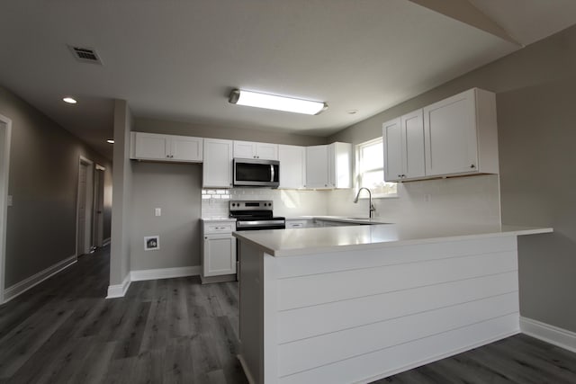kitchen featuring visible vents, a peninsula, baseboards, dark wood-style floors, and appliances with stainless steel finishes