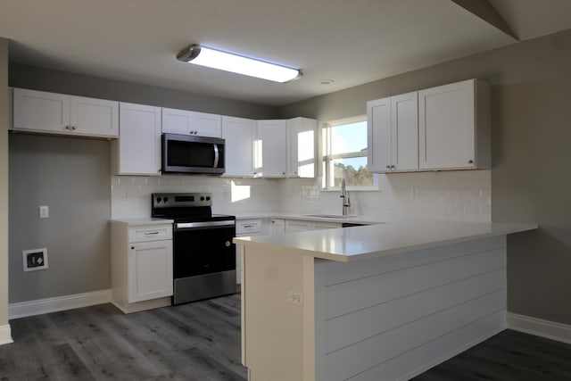 kitchen with appliances with stainless steel finishes, light wood finished floors, a peninsula, baseboards, and white cabinetry
