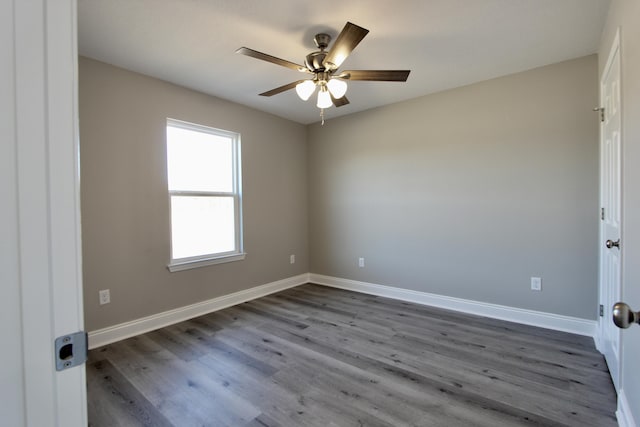 empty room featuring dark wood-type flooring, a ceiling fan, and baseboards