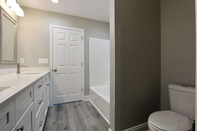 bathroom featuring double vanity, wood finished floors, a sink, a bathing tub, and toilet