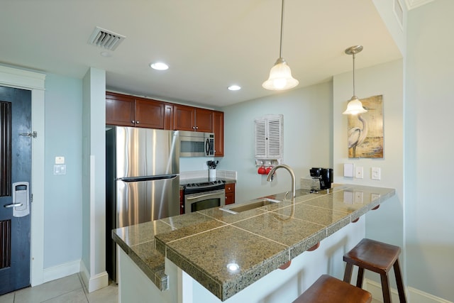 kitchen featuring visible vents, a peninsula, tile counters, a sink, and stainless steel appliances
