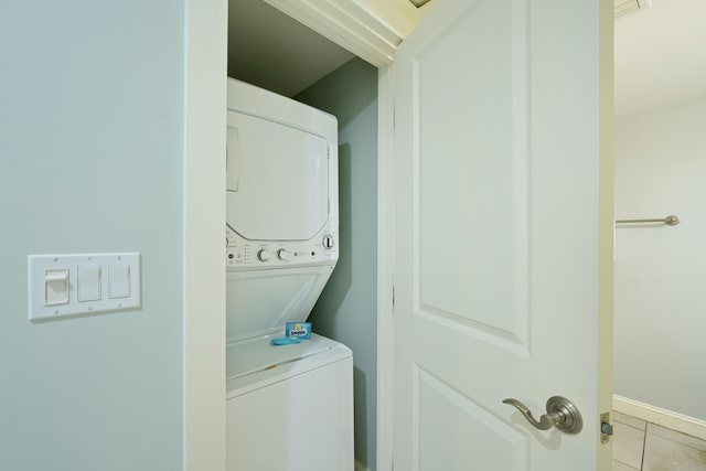 laundry area with baseboards, stacked washer and dryer, laundry area, and light tile patterned flooring