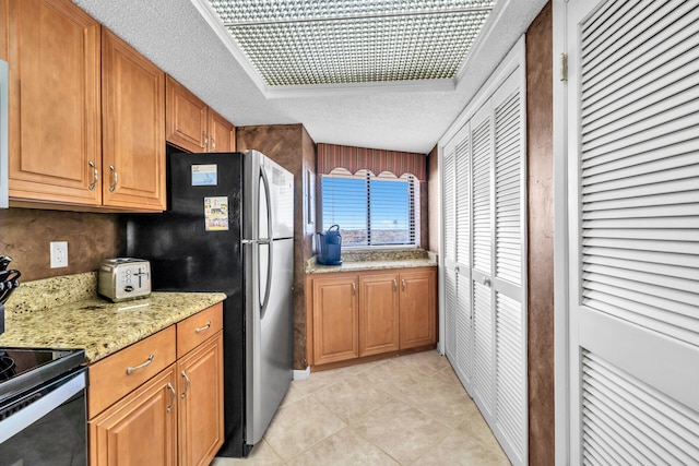 kitchen featuring a textured ceiling, black / electric stove, light tile patterned floors, light stone countertops, and brown cabinets