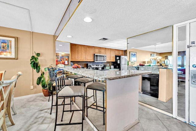 kitchen with appliances with stainless steel finishes, a peninsula, a breakfast bar area, a textured ceiling, and light stone counters