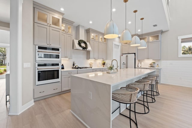kitchen with a breakfast bar area, visible vents, light wood-type flooring, white appliances, and wall chimney exhaust hood