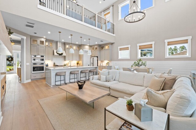 living area with a towering ceiling, visible vents, a chandelier, recessed lighting, and light wood-style flooring