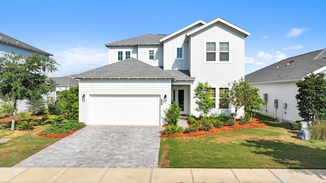 traditional home with roof with shingles, an attached garage, a front lawn, board and batten siding, and decorative driveway