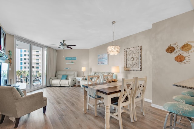 dining room featuring floor to ceiling windows, ceiling fan with notable chandelier, baseboards, and wood finished floors